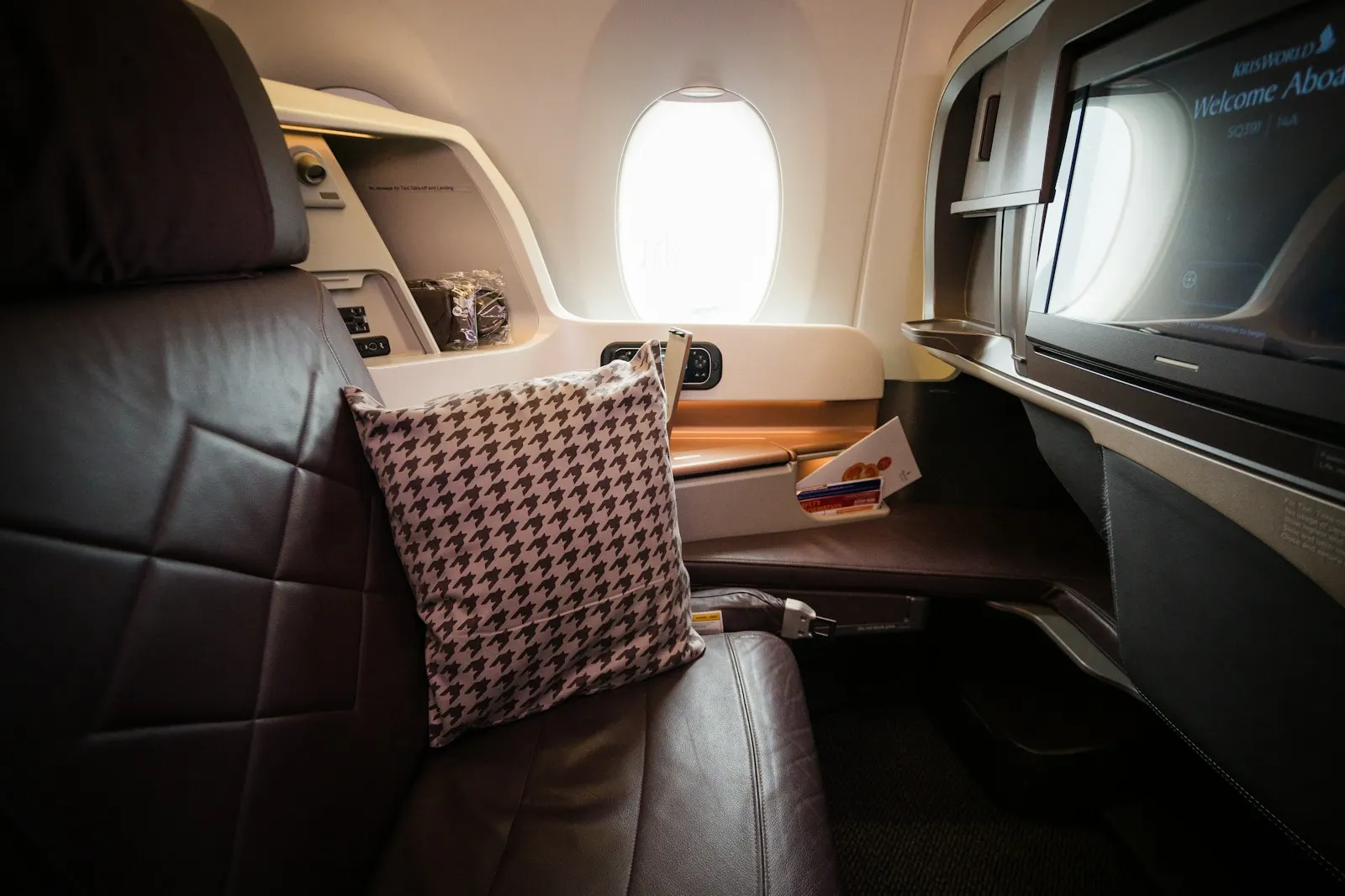 A business class seat with a pillow, a large screen and a window